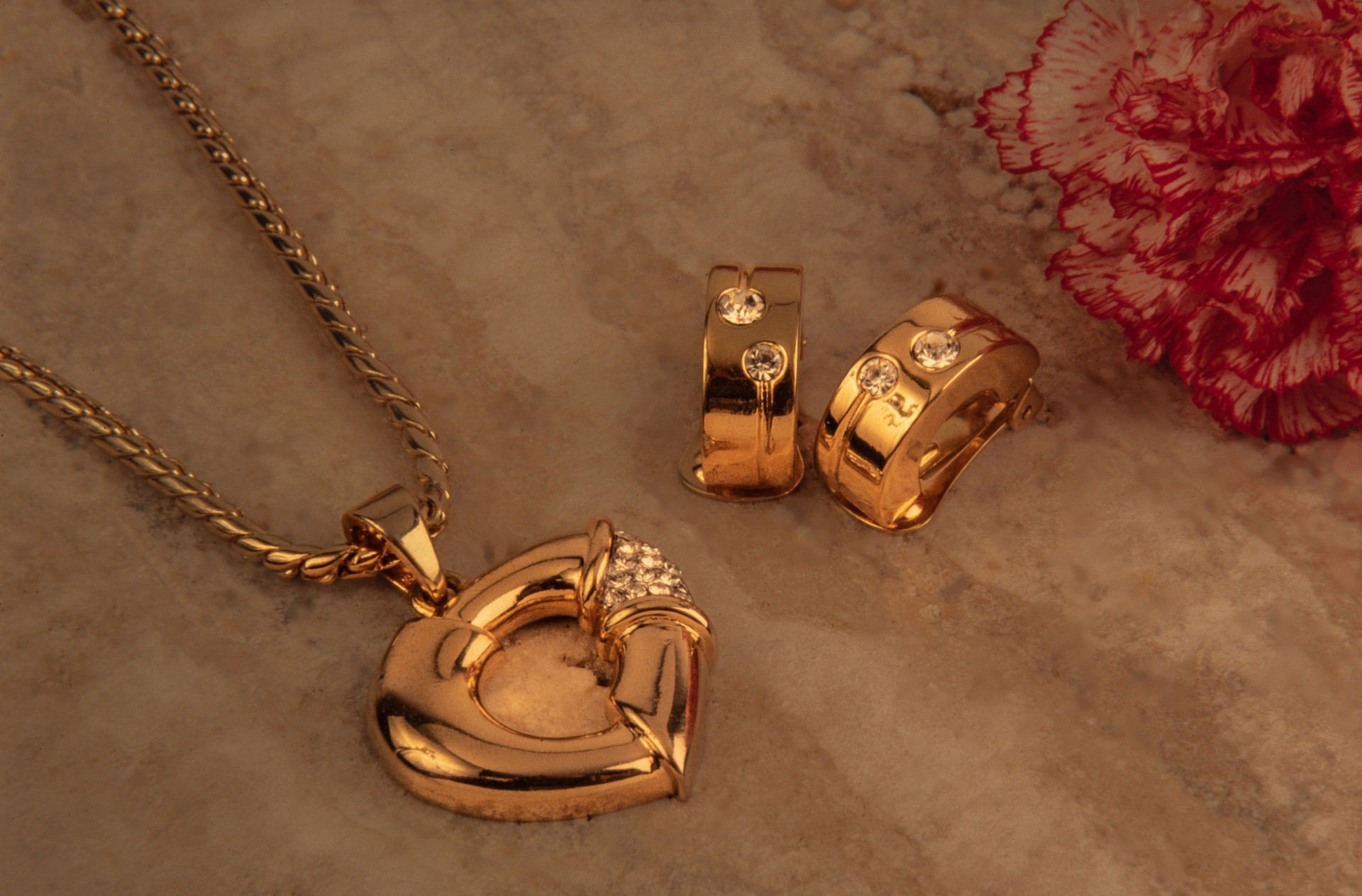 golden pendant on a stone background with a red carnation